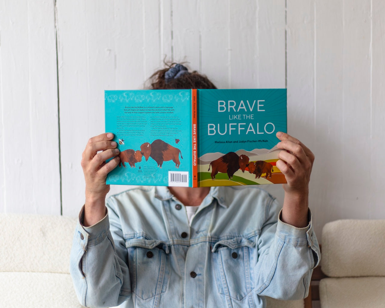 Someone holding the book Brave Like the Buffalo up in front of their face, showing the cover of the book.