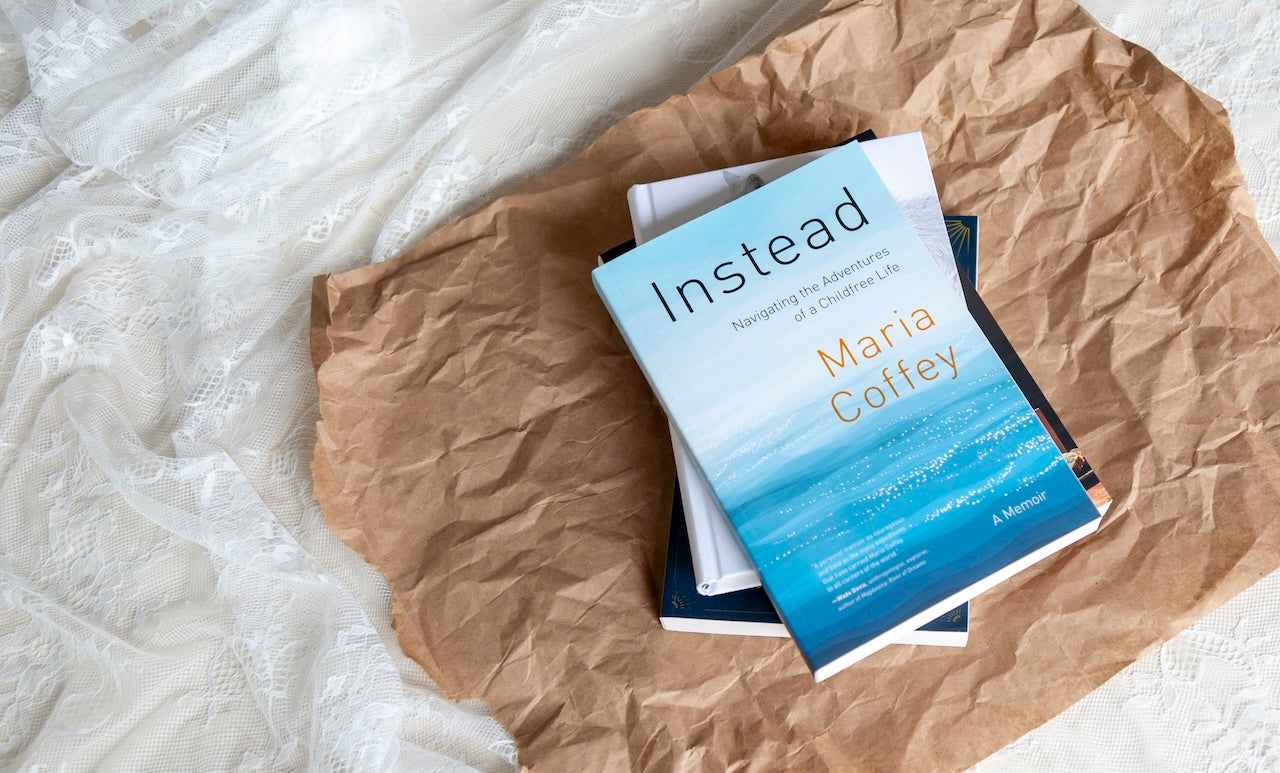 A photograph of books stacked on top of each other against some brown wrapping paper. The book on the very top of the pile is Instead by Maria Coffey. The image shows that these books will be given as a gift.